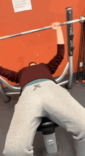 a man is laying on a bench lifting a barbell with the letter x on his pants