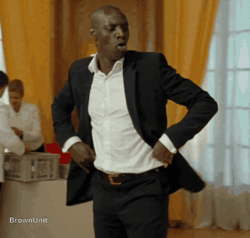 a man in a suit and white shirt is standing in front of a table with the words brownunit on it