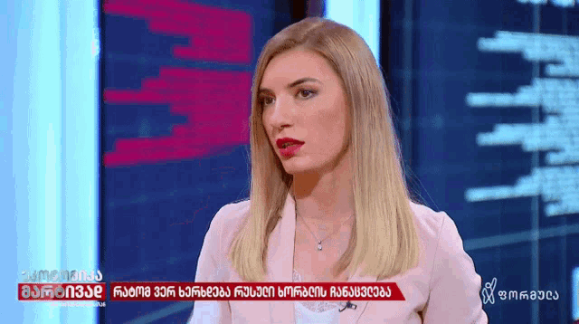 a woman in a pink jacket is on a television screen with a foreign language displayed above her