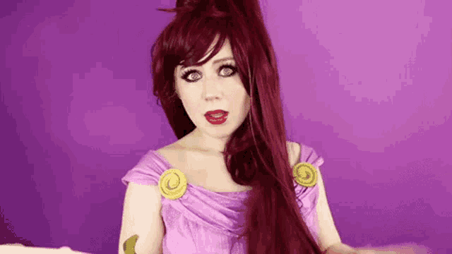 a woman in a purple dress and red hair is standing in front of a purple background .