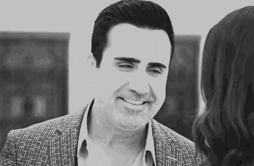 a man in a suit is smiling and looking at a woman .
