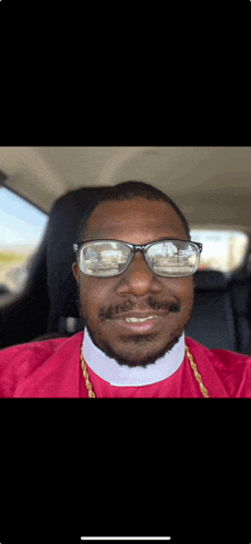 a man wearing sunglasses and a red robe is sitting in the back seat of a car .
