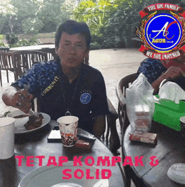 a man sitting at a table with a sign that says " tetap kompak & solid "