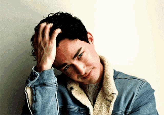 a man wearing a denim jacket and a sweater scratches his head