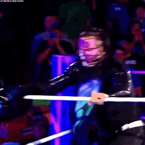 a wrestler is standing in front of a crowd in a ring .