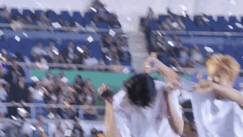 a group of people are dancing in front of a crowd in a stadium while confetti is being thrown in the air .