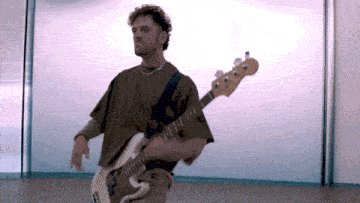 a man in a brown shirt is holding a white bass guitar