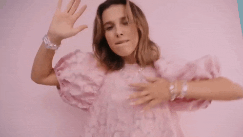 a woman in a pink dress is waving at the camera .