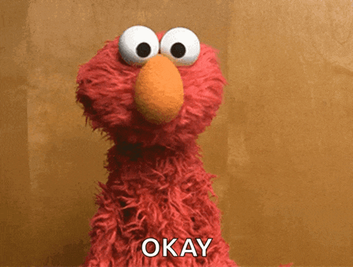 elmo from sesame street says " okay " in front of a brown wall