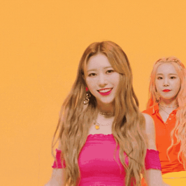 a woman in a pink top is dancing with another woman in an orange shirt behind her .