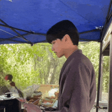 a man standing under a blue tent holding a book