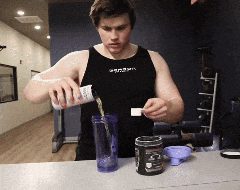 a man wearing a tank top that says dragon is pouring liquid into a container