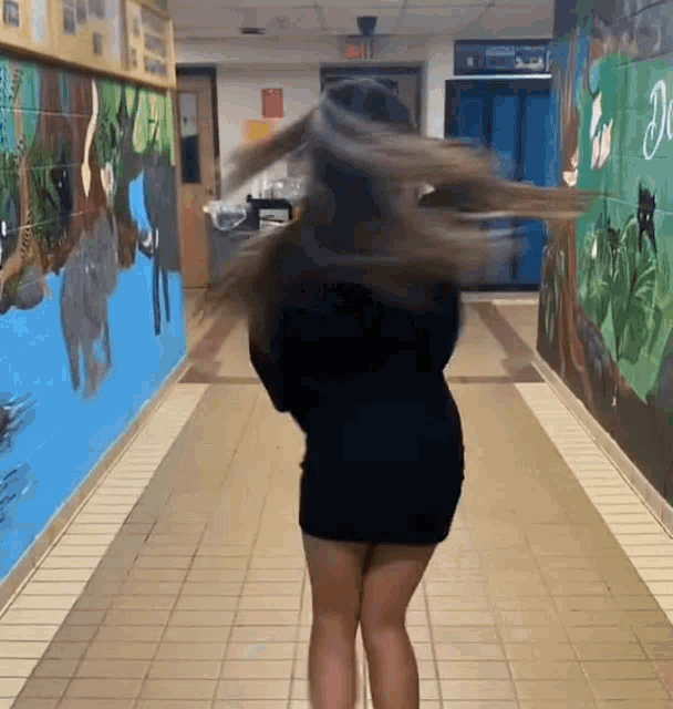 a woman in a black dress is standing in a hallway with her hair blowing in the wind .