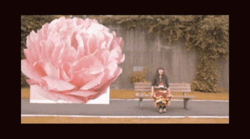 a woman is sitting on a bench next to a large pink flower