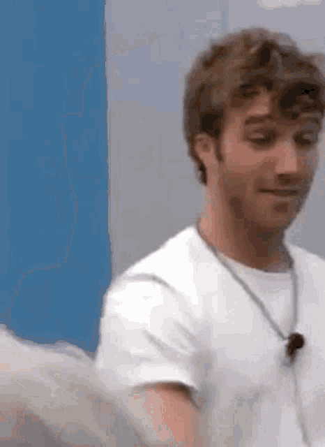 a man in a white shirt is standing in front of a blue wall and looking at the camera .