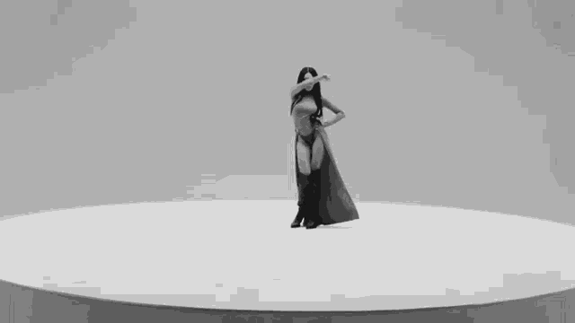 a black and white photo of a woman in a long dress dancing on a white circle .