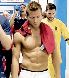 a shirtless man with a red towel around his neck is walking in a locker room