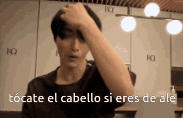 a man in a black shirt is touching his hair with the words tocate el cabello si eres de ale written below him