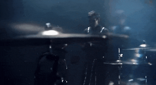 a man is playing drums in a dark room with smoke coming out of the drum set .
