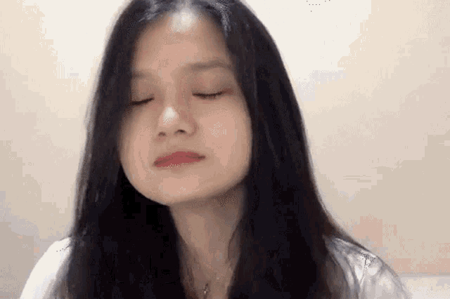 a young woman with long black hair is making a funny face with her eyes closed .