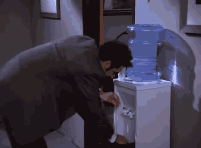 a man in a suit drinks water from a water cooler