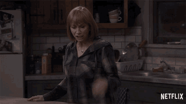 a woman in a plaid shirt is standing in a kitchen with a netflix logo in the corner