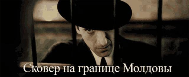 a man in a suit and hat is behind bars with the words skover na granice moldovs written below him