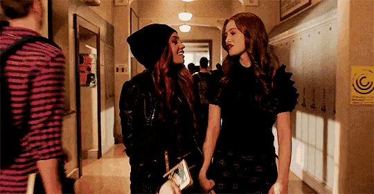 two girls are standing next to each other in a hallway holding hands .