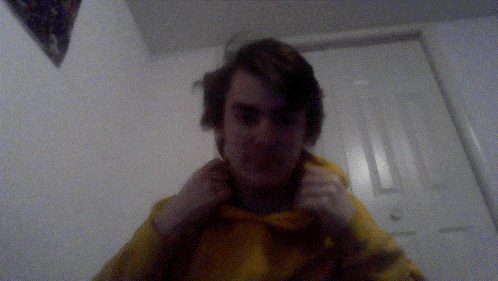 a young man wearing a yellow hoodie adjusts his collar