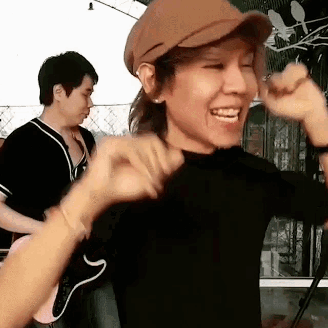 a woman wearing a hat is smiling and making a heart with her hands .
