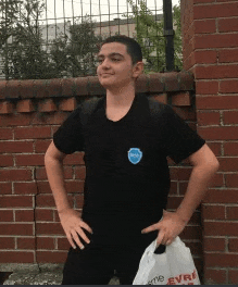 a young man in a black shirt is standing in front of a brick wall holding a bag that says evre