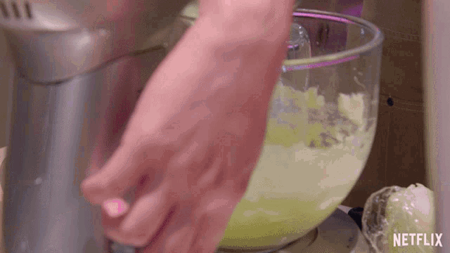 a person is mixing something in a mixer with netflix written on the bottom of the screen
