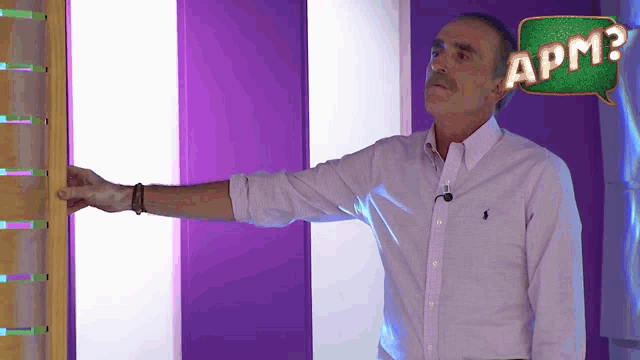 a man stands in front of a purple wall with a green speech bubble that says apm2