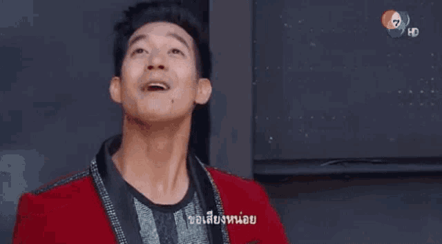 a man in a red jacket is singing into a microphone while looking up .