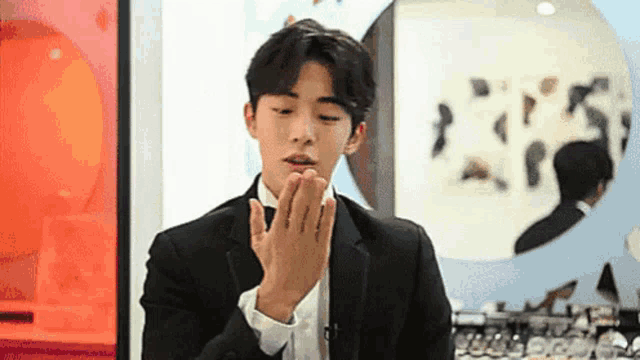 a man in a suit and bow tie is holding his hands together in front of a mirror .