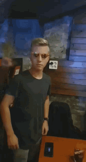 a man wearing sunglasses is standing in front of a table with a cell phone on it