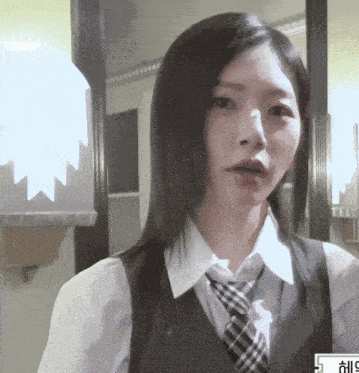 a woman wearing a white shirt and a black vest with a plaid tie is looking at the camera