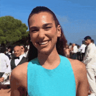 a woman in a blue dress is smiling while standing in front of a crowd of people .