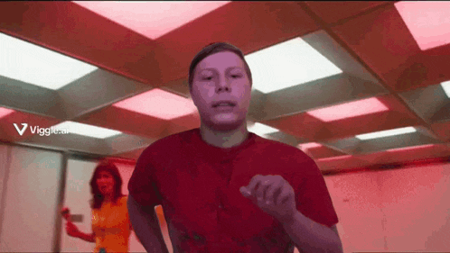 a man in a red shirt is running in a room with a woman in a yellow shirt behind him .