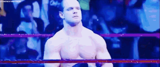 a shirtless wrestler is standing in a wrestling ring with a crowd watching .
