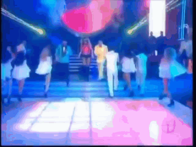a group of people are dancing on a stage in front of a large screen