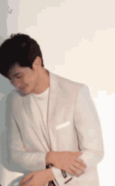 a man in a white suit and white shirt is adjusting his cufflinks .
