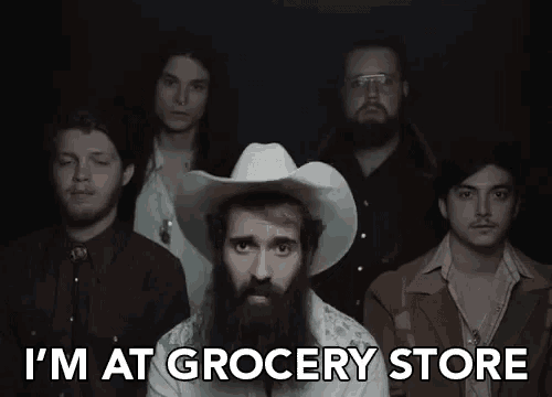 a man in a cowboy hat is standing in front of a group of men and says i 'm at grocery store