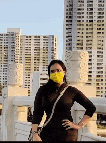 a woman wearing a yellow face mask stands on a bridge in front of tall buildings