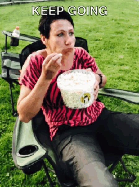 a woman is sitting in a chair eating a bowl of popcorn