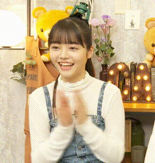 a girl in overalls is clapping her hands in a room with stuffed animals and flowers .