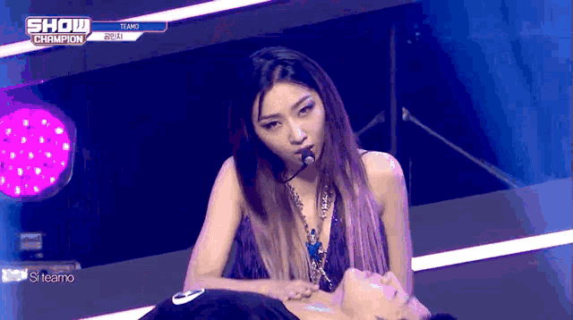 a woman singing into a microphone while laying on a man 's stomach during a show champion performance