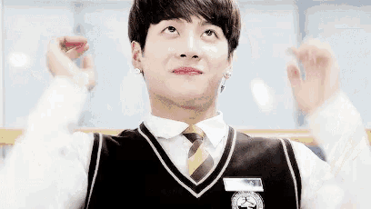 a young man wearing a vest and tie is making a funny face