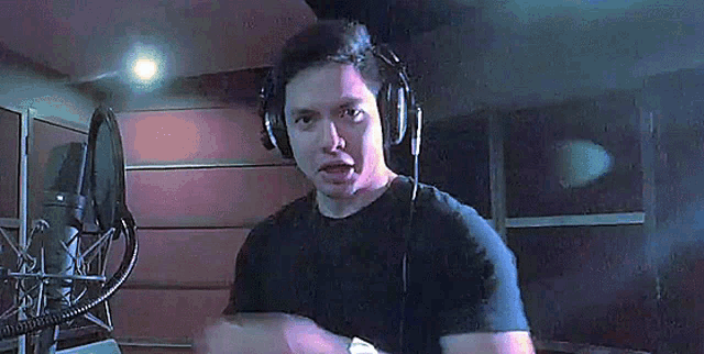 a man wearing headphones and a black shirt is standing in front of a microphone .
