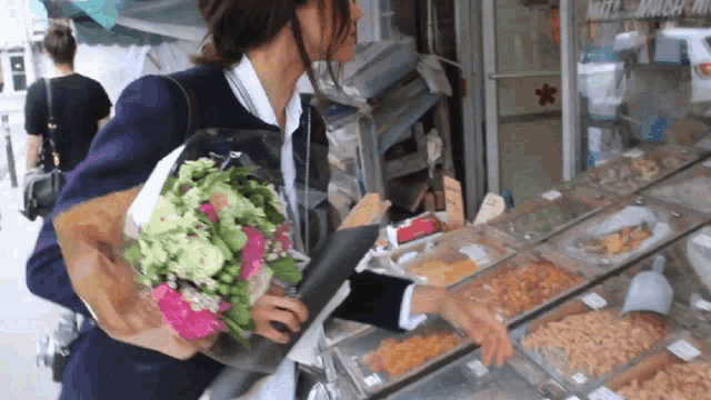 a woman is holding a bouquet of flowers in front of a nuts and snacks display